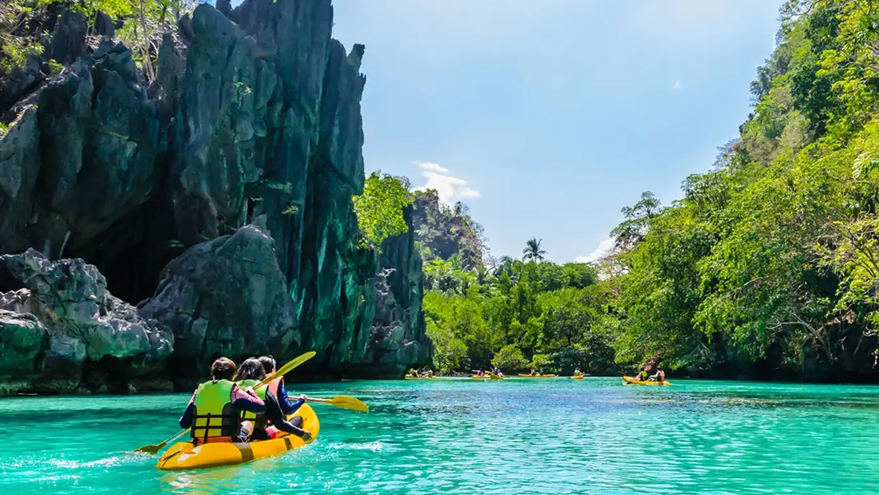 Tandem kayakers in a yellow kayak entering a karst-walled lagoon in El Nido