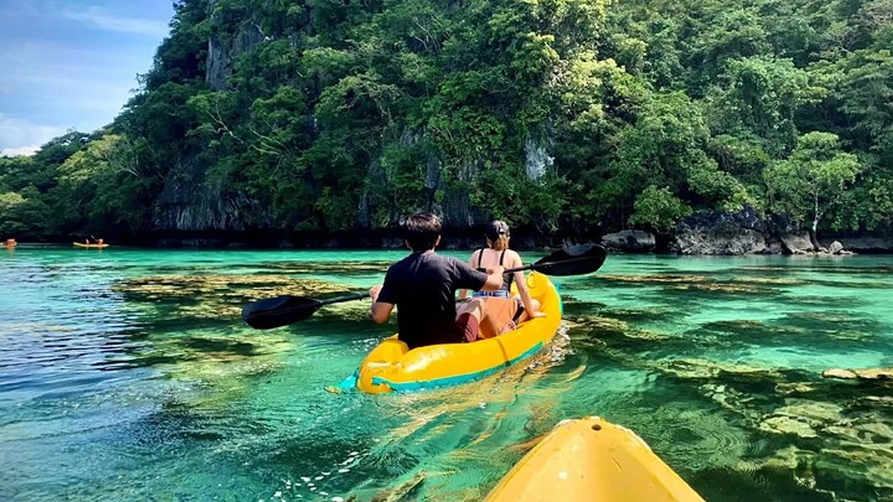 Two paddlers in a yellow kayak over coral shallows, photographed from a following kayak