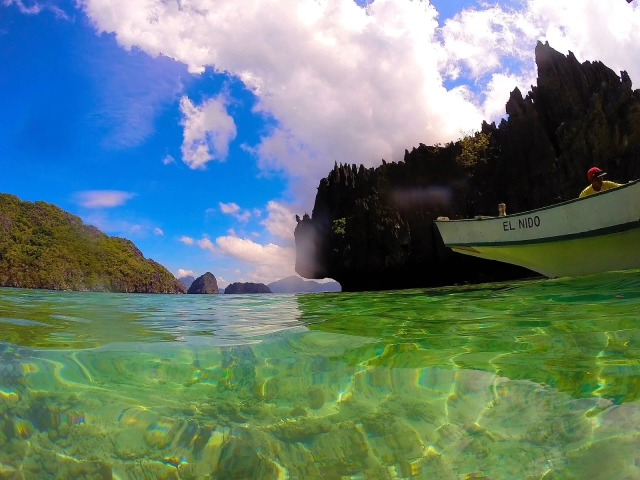 Half-underwater view of karst islets with an outrigger boat marked El Nido