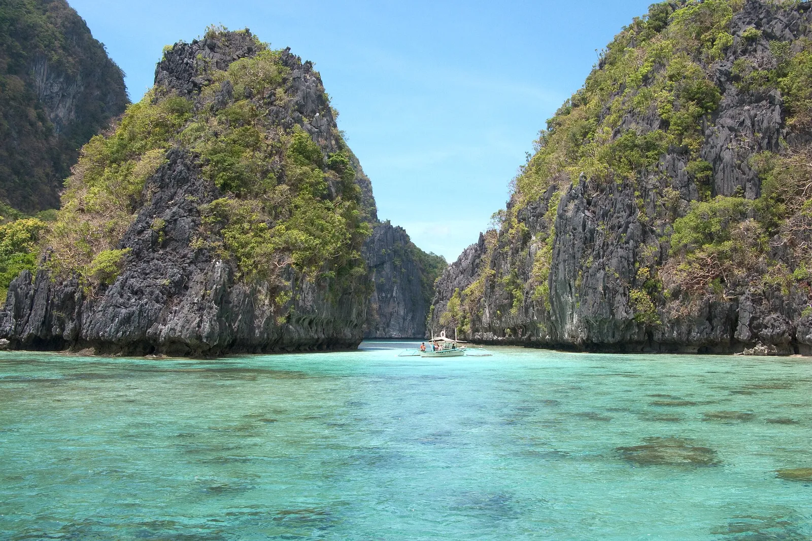 Outrigger boat in a shallow turquoise lagoon between karst outcrops in Bacuit Bay, El Nido