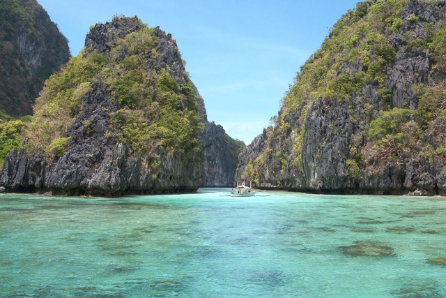 Outrigger boat in a shallow turquoise lagoon between karst outcrops in Bacuit Bay, El Nido