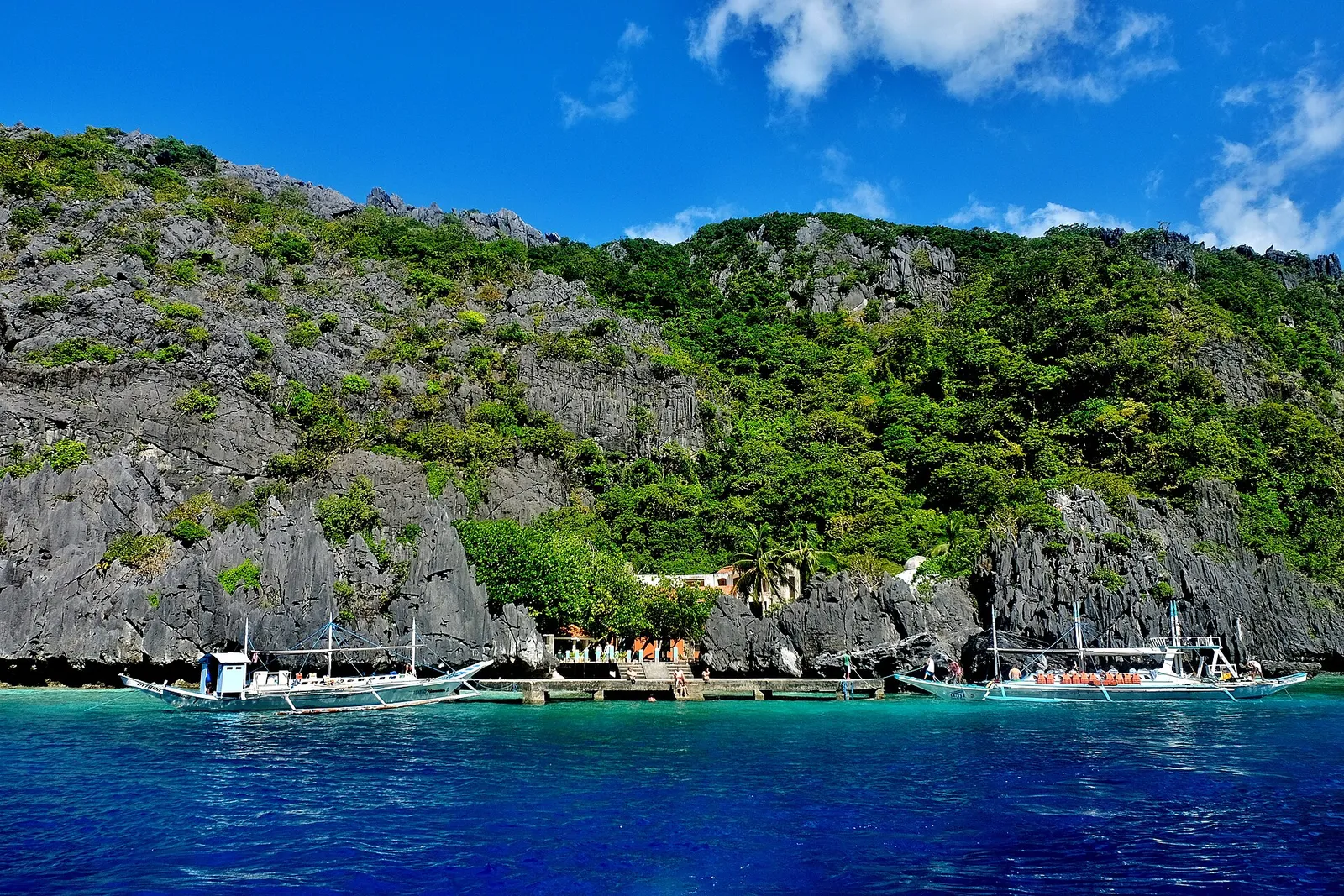Two outrigger boats moored at the stone jetty below karst cliffs at Matinloc Shrine, El Nido