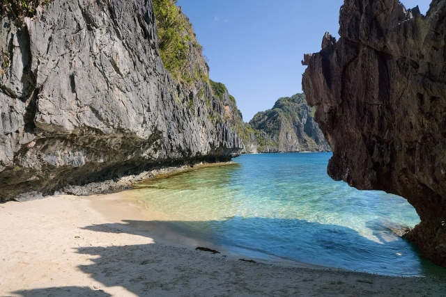 Sheltered white-sand cove framed by a rock arch and cliff on Matinloc Island, El Nido
