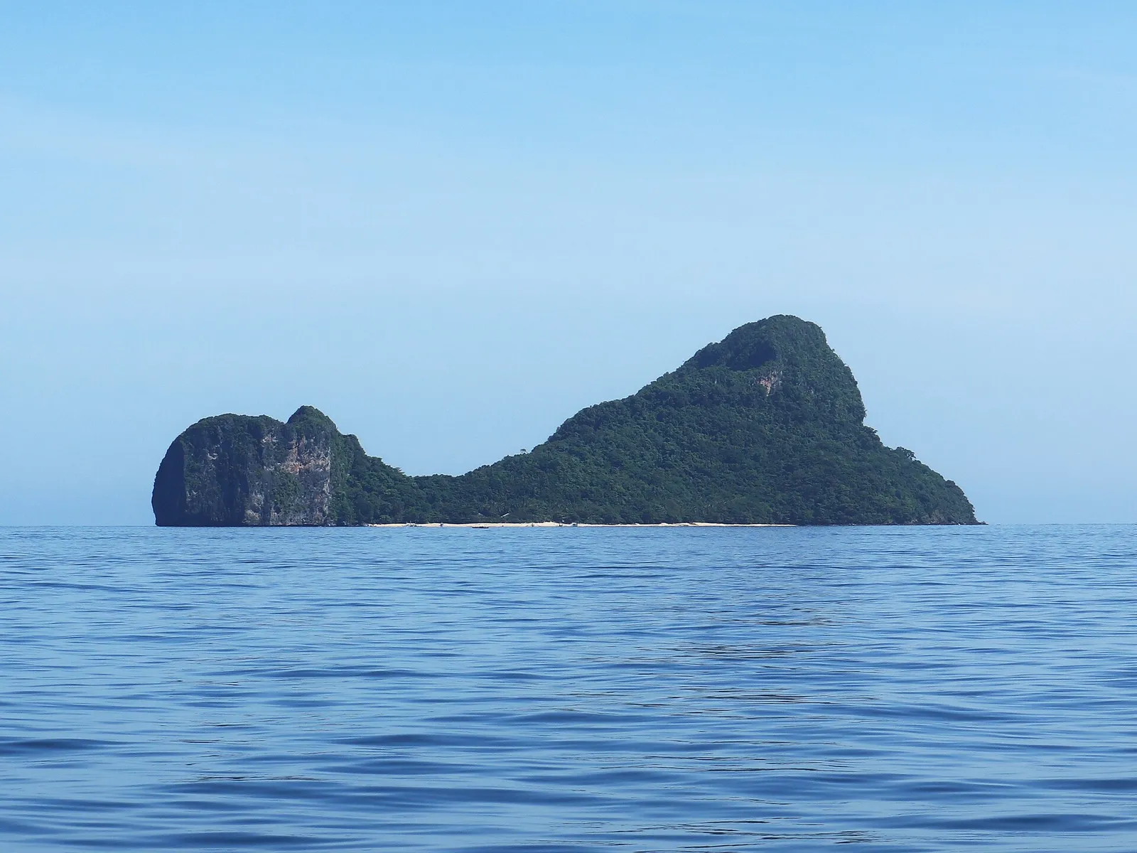 A lone karst island with cliffs and a sliver of beach on open sea in Palawan