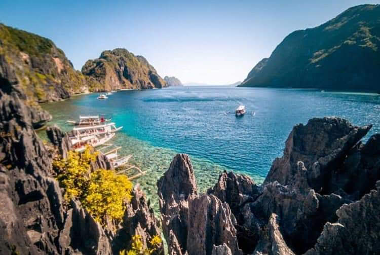 View from a jagged karst ridge over a strait with tour boats moored below, El Nido
