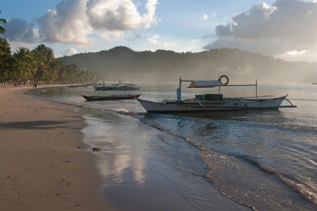 Outrigger boats beached on the curving sand at Port Barton at golden hour