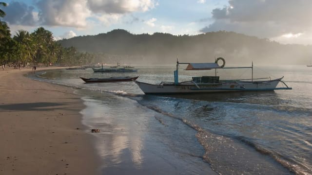Outrigger boats beached on the curving sand at Port Barton at golden hour