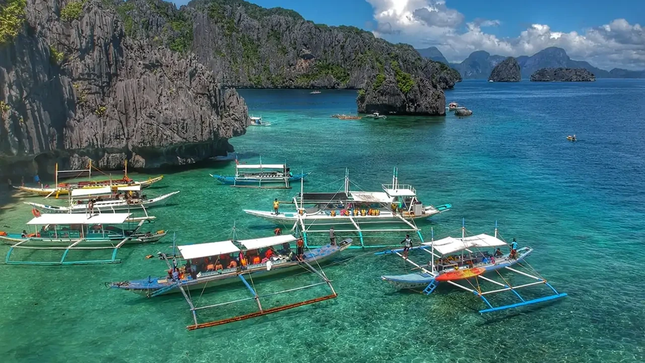 Tour bangkas loaded with passengers moored along a karst shoreline in El Nido
