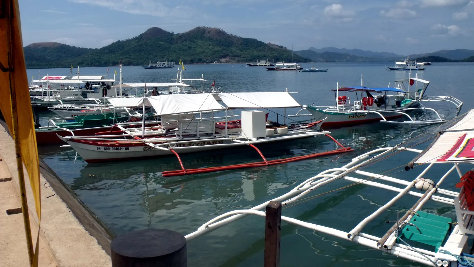 Outrigger bancas moored along the town pier in Coron, with green hills across the bay