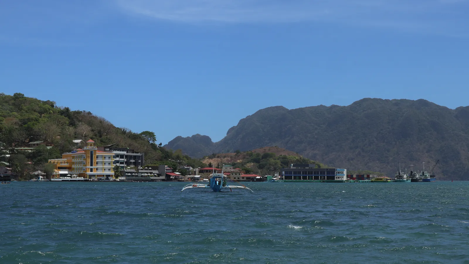 Arriving at Coron town by sea, with a banca in the foreground, waterfront buildings and the mountains of Busuanga behind