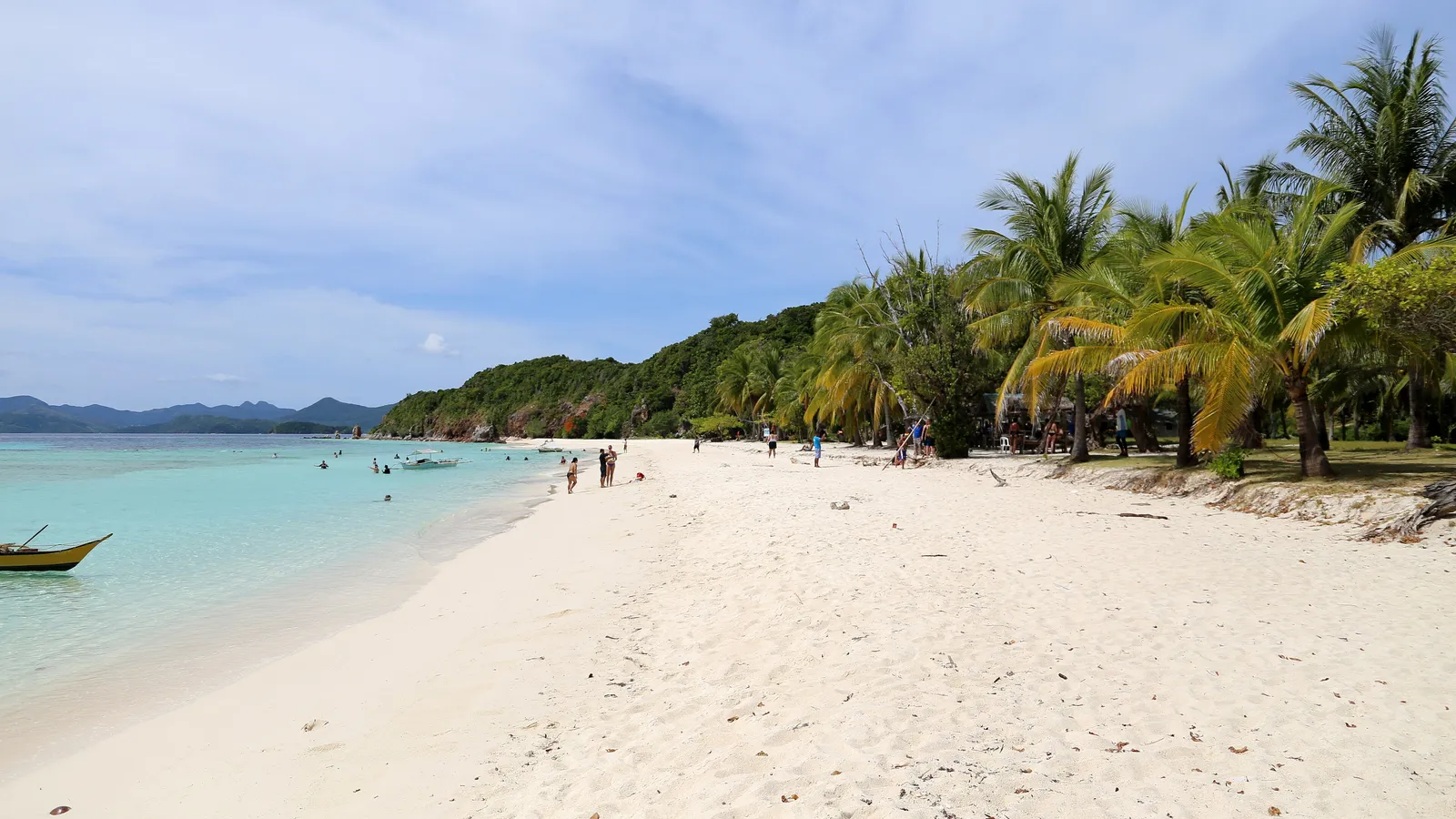 Long white-sand beach lined with coconut palms beside shallow turquoise water, Malcapuya Island, Coron