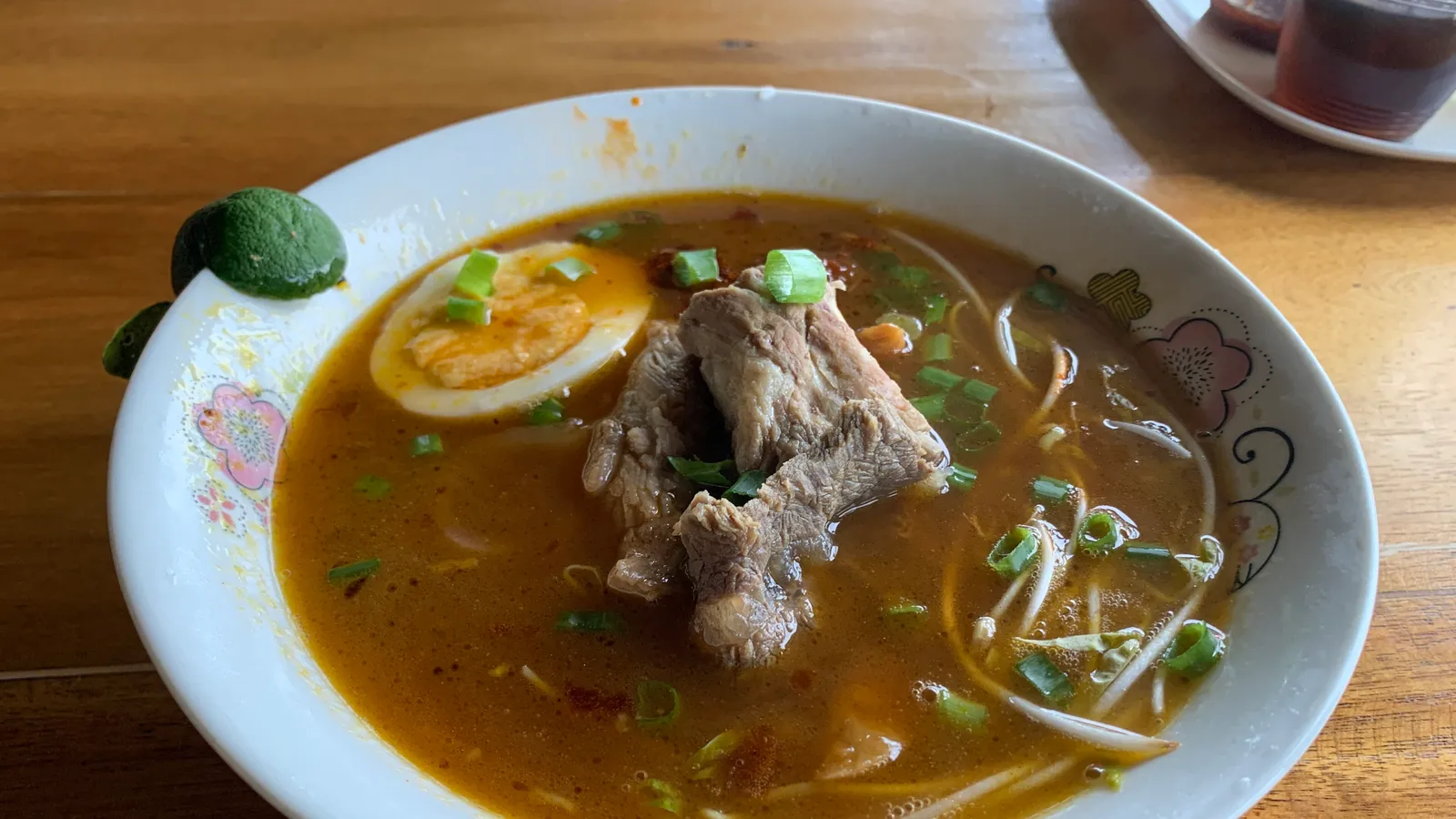 A bowl of Puerto Princesa chaolong: beef noodle soup with a halved egg, spring onions and calamansi