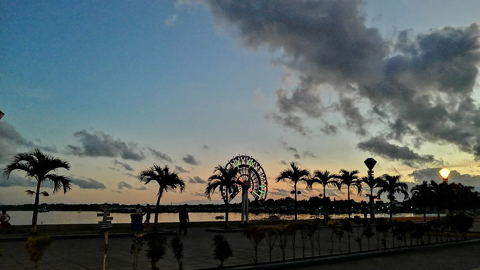 Palm-lined Puerto Princesa Baywalk against a dramatic sky, with its lit Ferris wheel by the bay