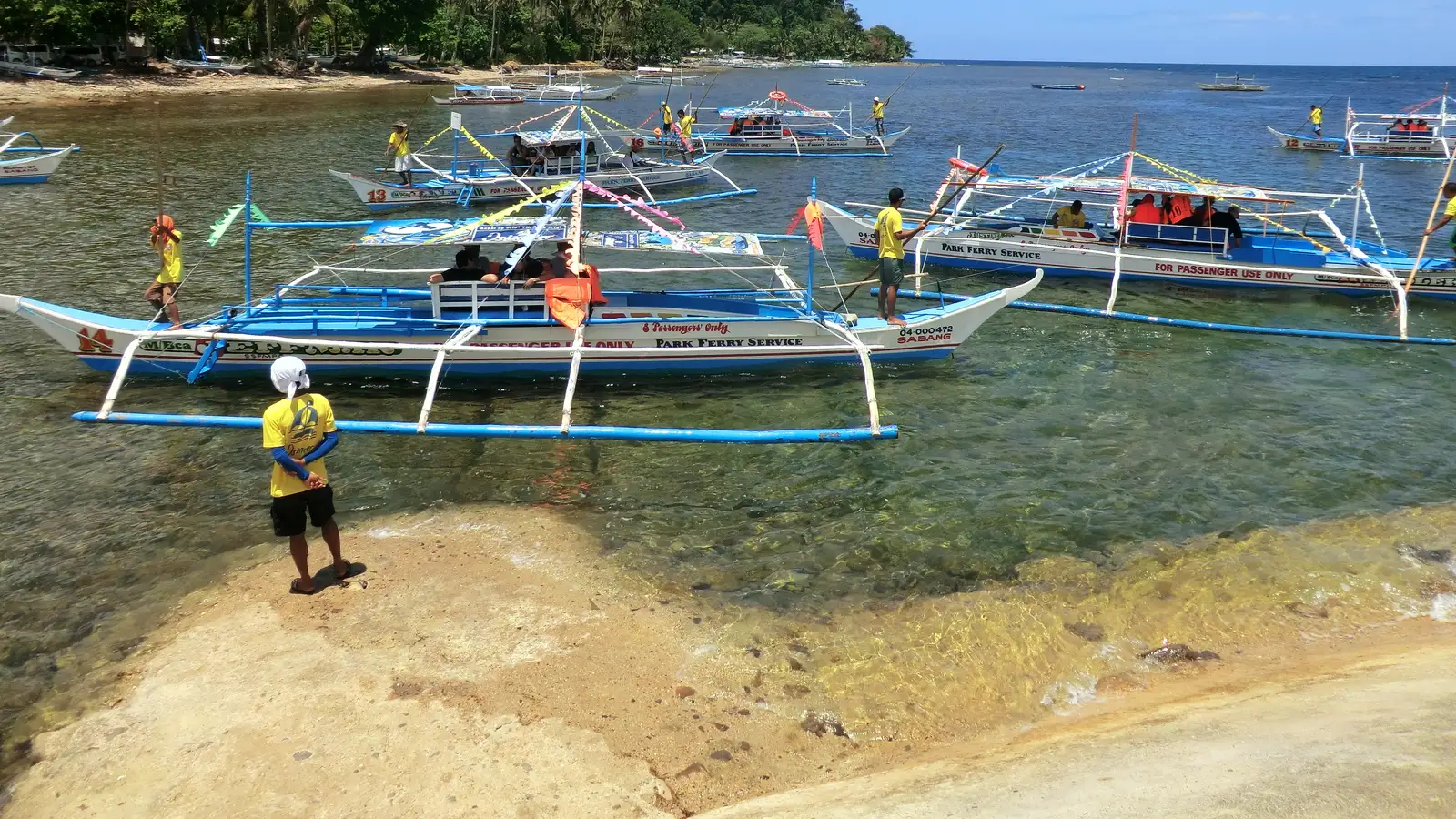 Outrigger bancas moored in the shallows at Sabang, with boatmen loading visitors for the Underground River trip